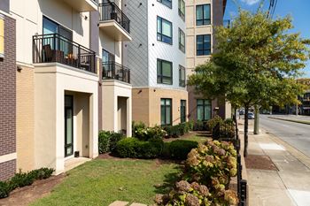 A row of apartment buildings with balconies and green bushes in front.
